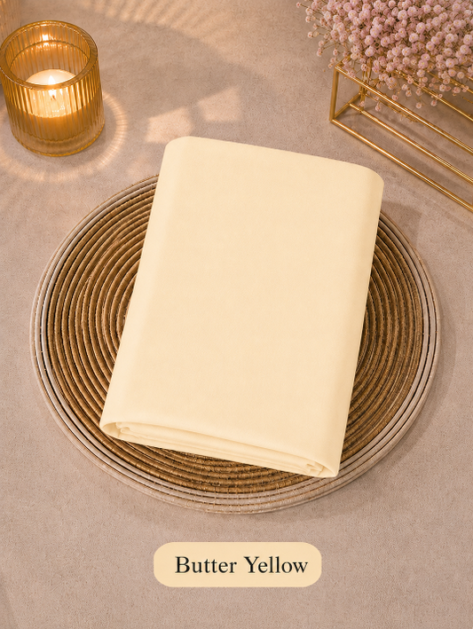 Butter yellow folded Liquid Chiffon Hijab fabric on a woven coaster with a candle and decorative elements in the background.