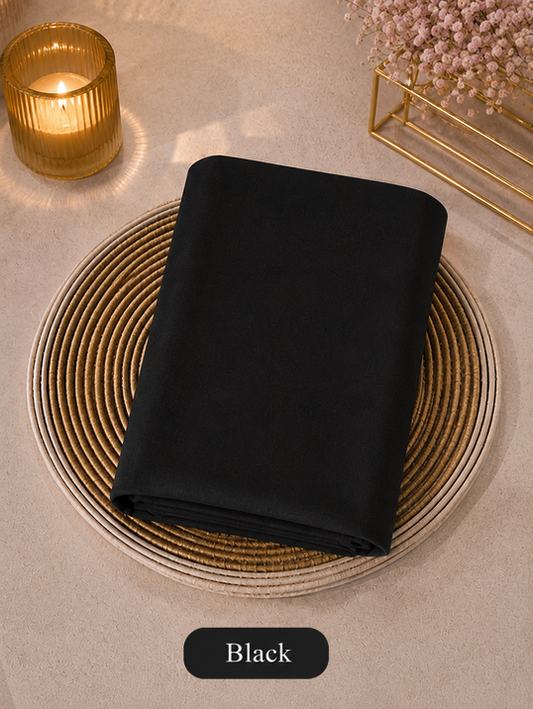 Black folded Liquid Chiffon Hijab fabric on a woven mat with a candle and flowers in the background