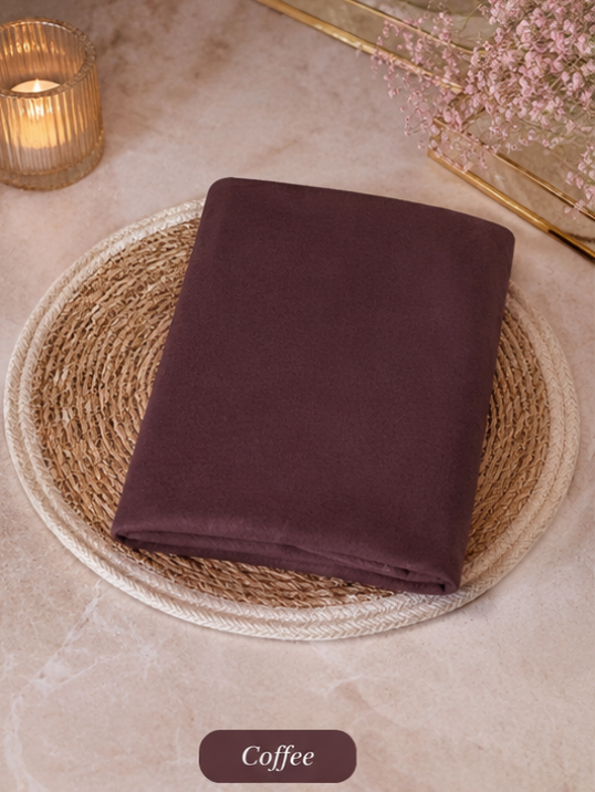 Folded dark brown Liquid Chiffon Hijab fabric on a woven mat with a candle and flowers in the background
