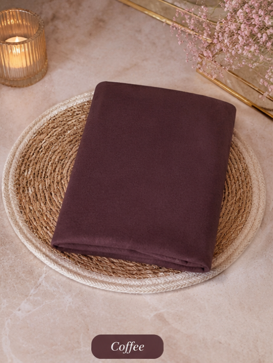 Folded dark brown Liquid Chiffon Hijab fabric on a woven mat with a candle and flowers in the background