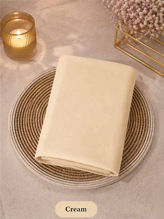 Cream-colored Liquid Chiffon Hijab folded fabric on a woven mat with a candle and decorative elements in the background.