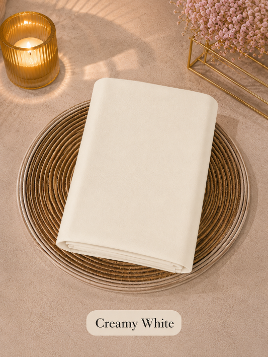 Folded creamy white -colored Liquid Chiffon Hijab on a woven placemat with a candle and flowers in the background.