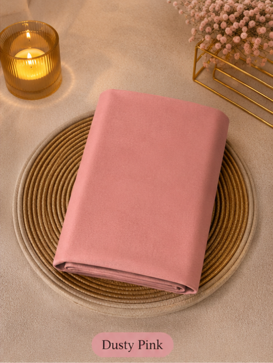 Folded dusty pink liquid chiffon hijab on a woven mat with a candle and decorative elements in the background.