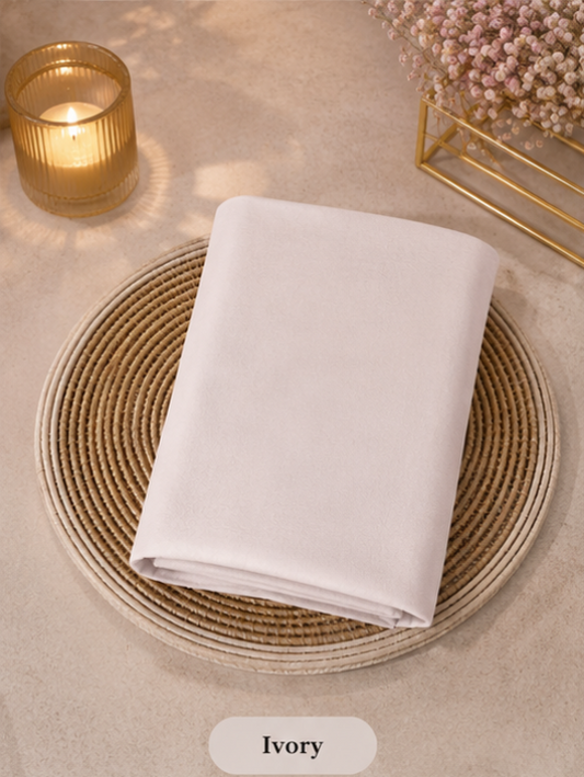 Ivory Liquid Chiffon Hijab on a woven placemat with a candle and flowers in the background