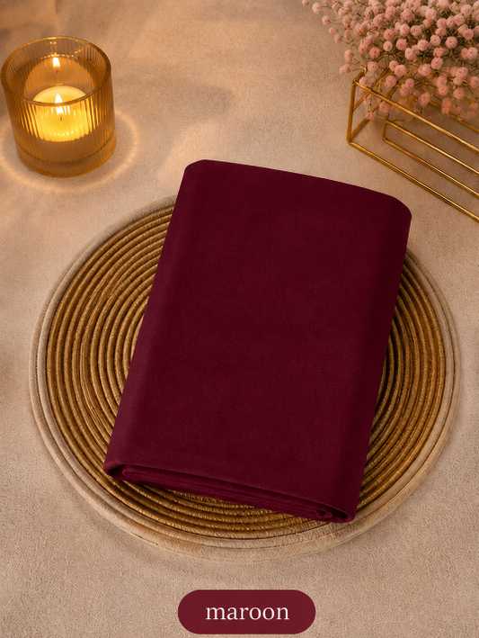Maroon Liquid chiffon Hijab on a woven placemat with a candle and decorative elements in the background.