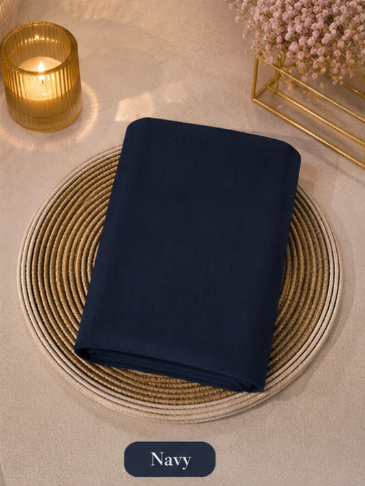 Navy Blue folded Liquid chiffon Hijab on a woven mat with a candle and flowers in the background