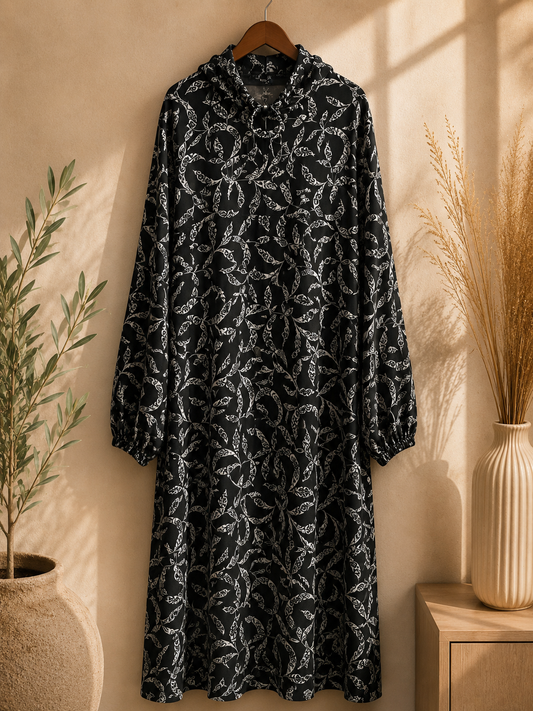 Premium Black and white patterned Islamic prayer and namaz dress on a hanger against a neutral wall with a plant and vase in the background.