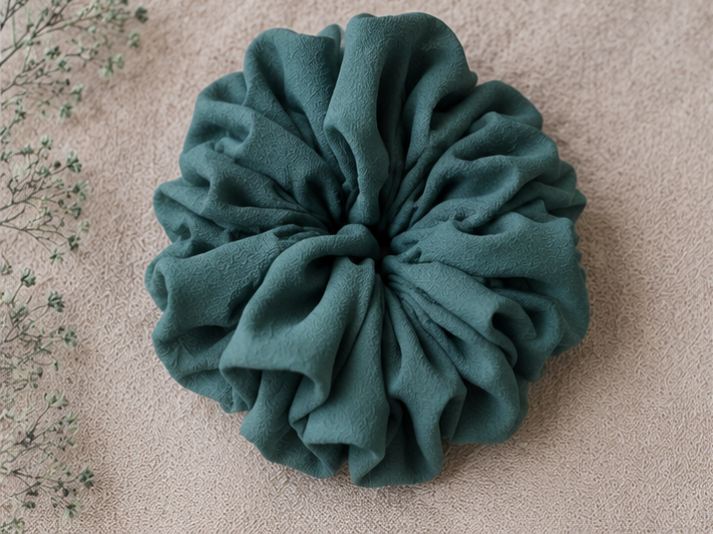 Dark Green scrunchie on a beige surface with a blurred natural background