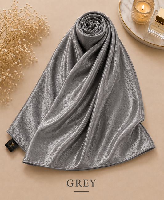 Rolled-up gray Bubble Satin Islamic Hijab Scarf on a beige surface with decorative elements.