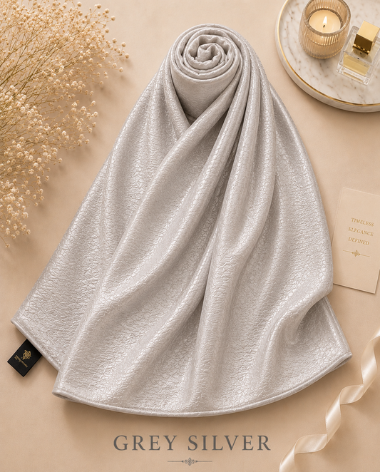 Rolled-up gray silver Bubble Satin Islamic Hijab Scarf on a beige surface with decorative elements.