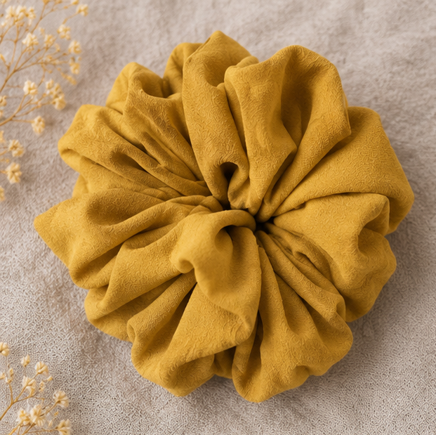 Mustard yellow scrunchie on a textured beige background with dried flowers.