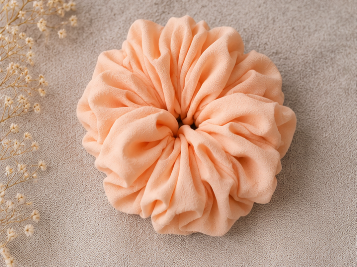 Pink Peach scrunchie on a textured beige surface with dried flowers.