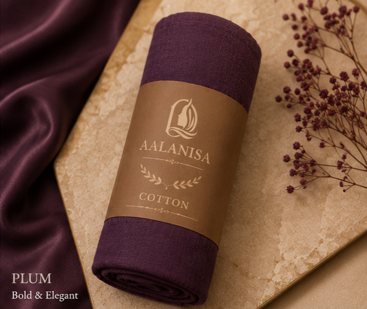 Rolled-up plum-colored Premium Cotton Hijab with Aalanisa branding on a textured surface with purple fabric and dried flowers.